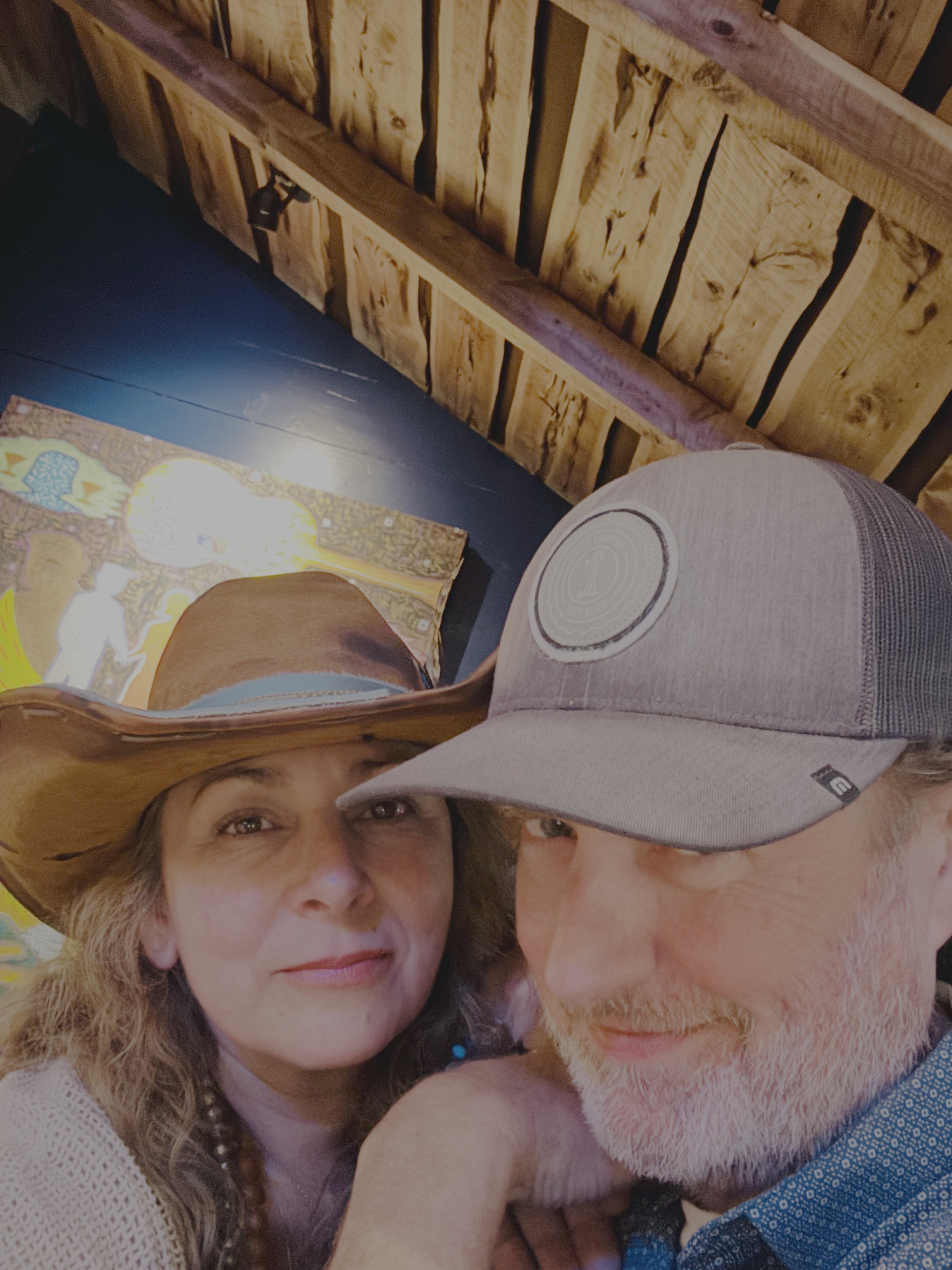 Alison McLaughlin, Texas Hill Country REALTOR and founder of Root and Roam Living, smiling in a wide-brim hat next to her husband Lance under a rustic wood-beam ceiling